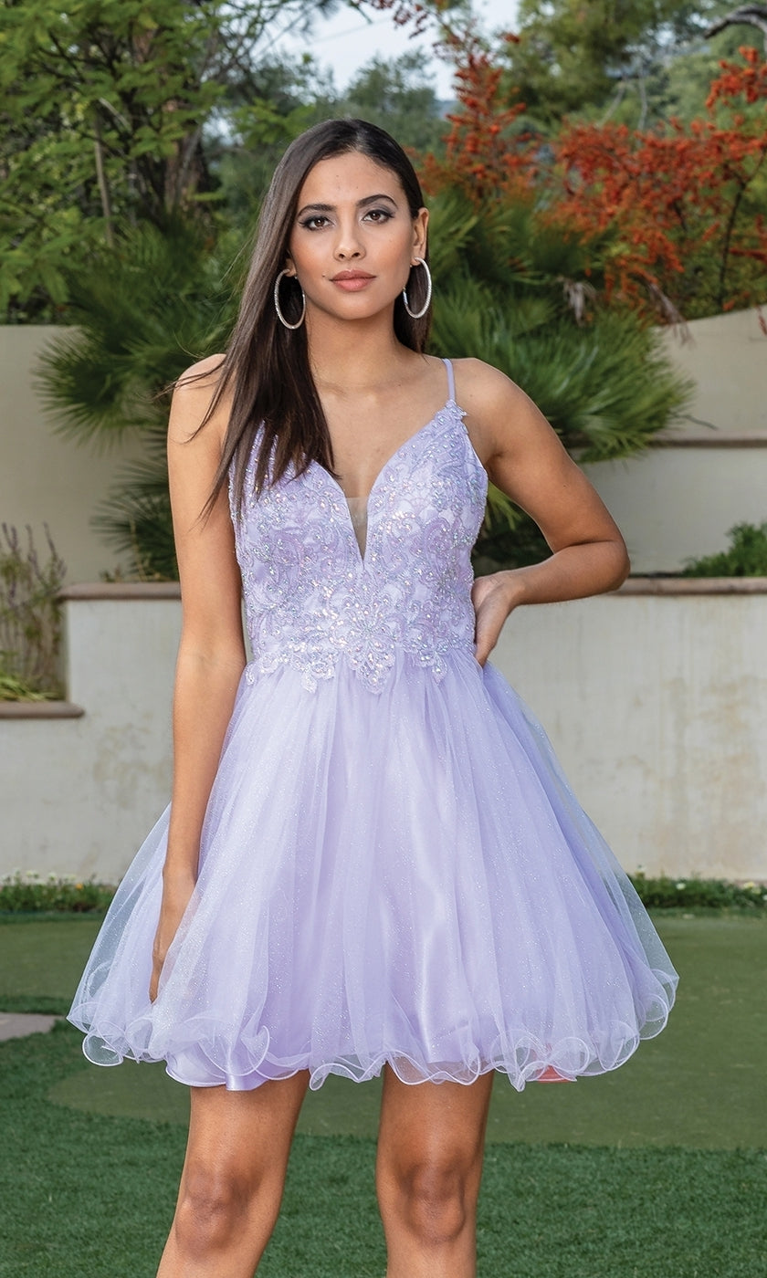 A young woman wears the Short Babydoll Homecoming Dress with Beading, featuring a light purple fitted bodice and flared tulle skirt, standing outdoors by greenery and a beige wall.